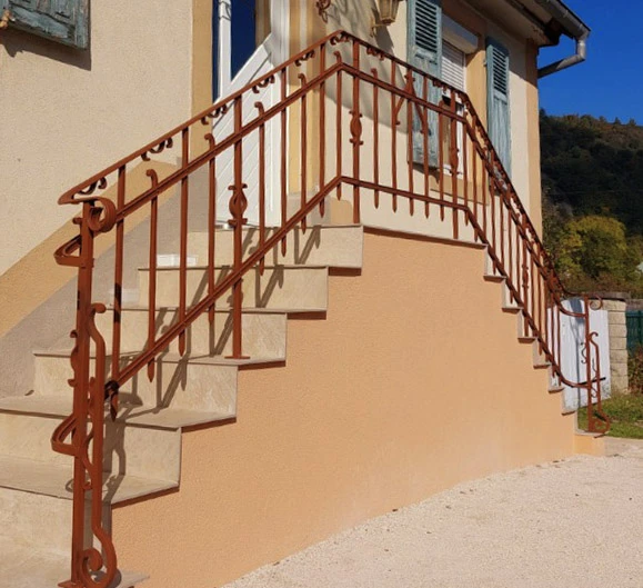 Escalier extérieur en béton avec rampe métallique rouge ornementale menant à l'entrée d'une maison