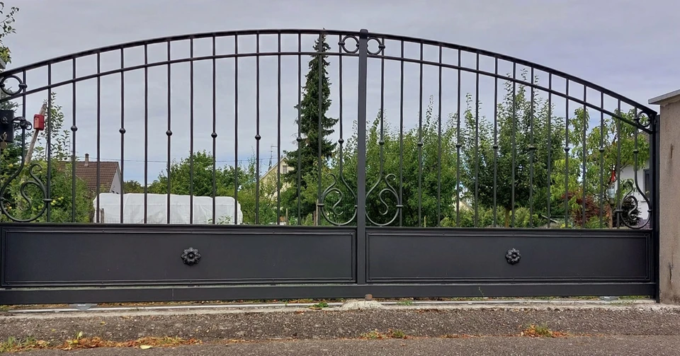 Entrée de propriété rustique au crépuscule avec portail en bois à lames verticales, éclairage d'ambiance chaleureux