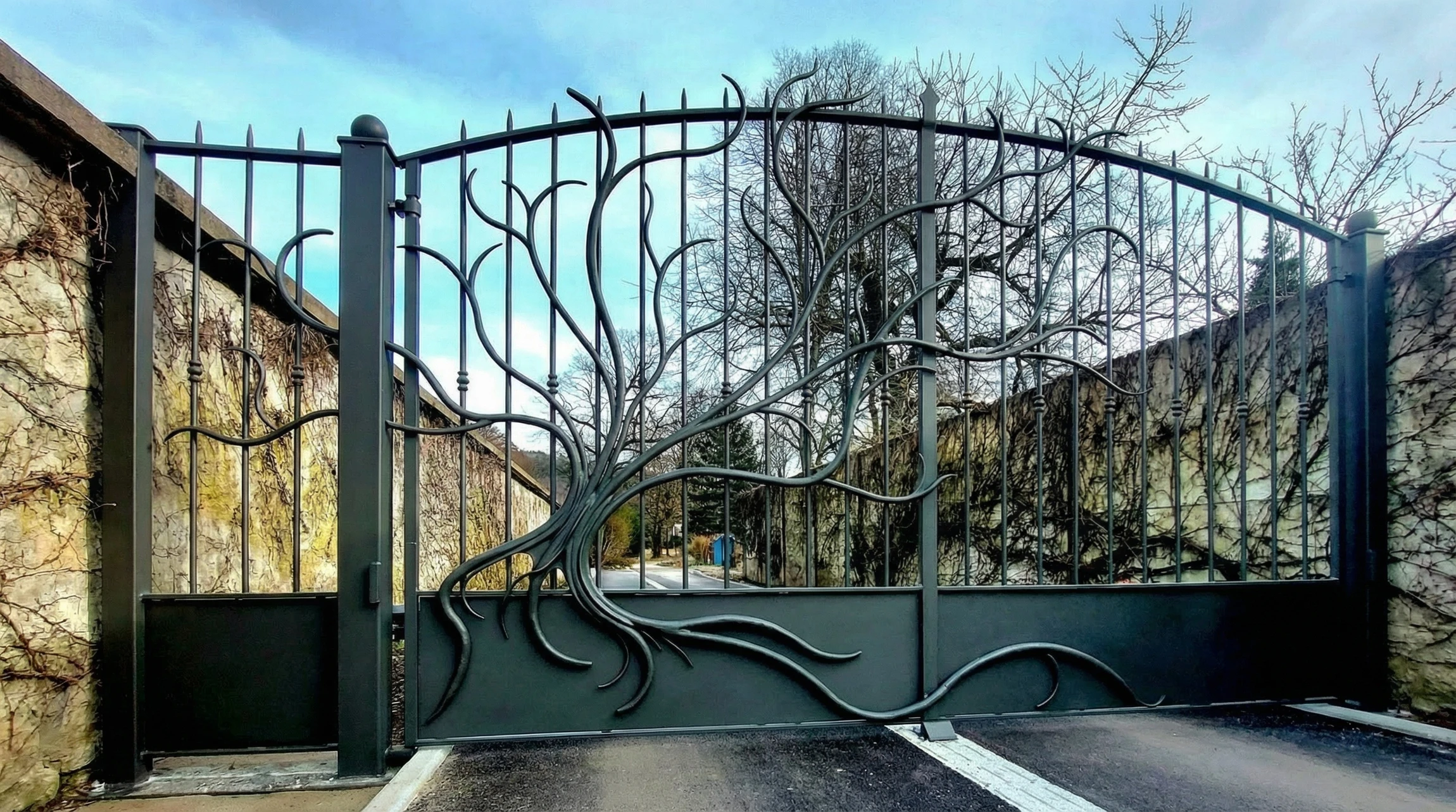 Portail en fer forgé rouge avec ornements spiralés et serrure dorée, donnant accès à un campus universitaire