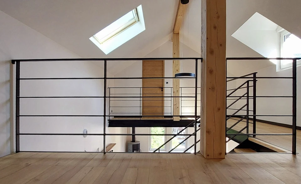 Façade résidentielle avec balcon en fer forgé noir à barreaux courbes, murs crépi beige, toiture ardoise grise, fenêtres blanches à petits carreaux, luminaires muraux style lanterne