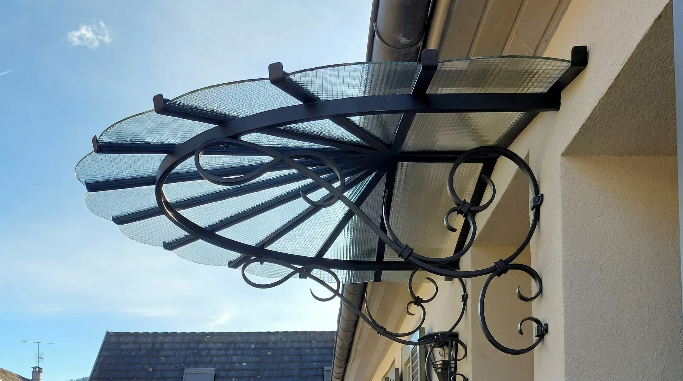 Scène extérieure dans jardin avec serre victorienne ornementale en métal peint bleu-gris, structure arquée avec verrières et portes vitrées ouvertes