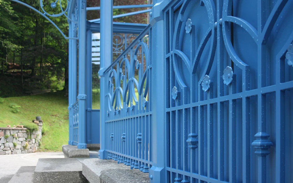 Vue depuis l'intérieur d'une habitation à travers une fenêtre ouverte avec garde-corps décoratif en fer forgé blanc à motifs ornementaux