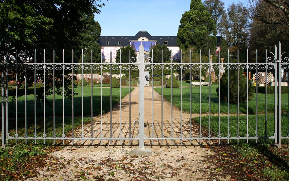 Vue depuis l'intérieur d'une habitation à travers une fenêtre ouverte avec garde-corps décoratif en fer forgé blanc à motifs ornementaux